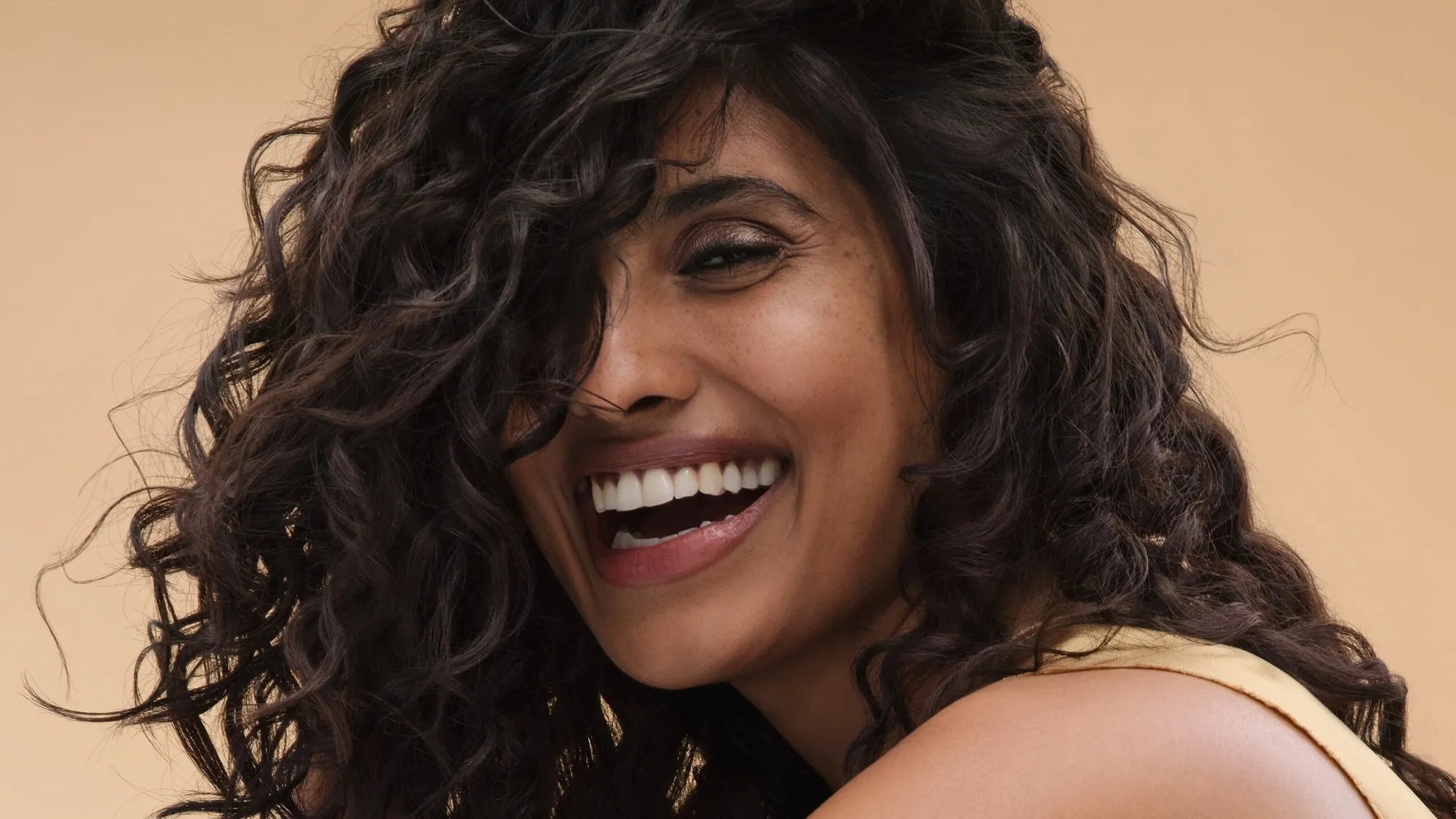 Model with dark brown, glossy, frizz-free curls smiles at camera.