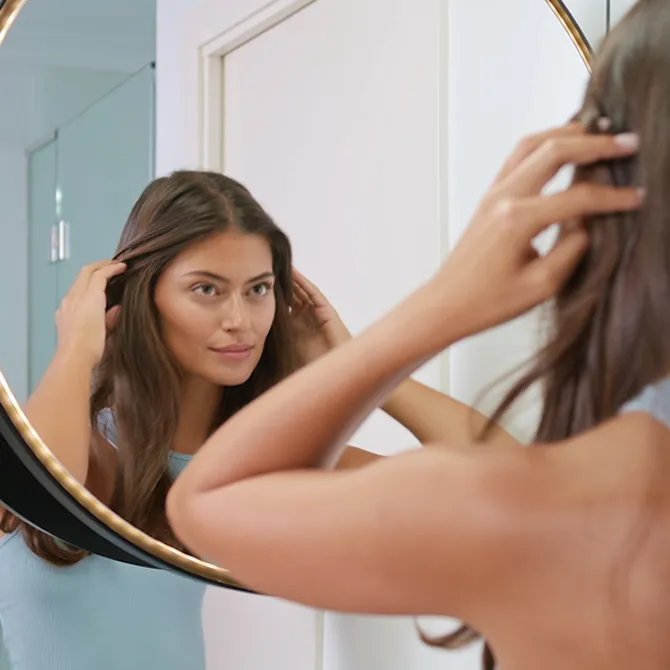  Model looks in mirror while styling hair.