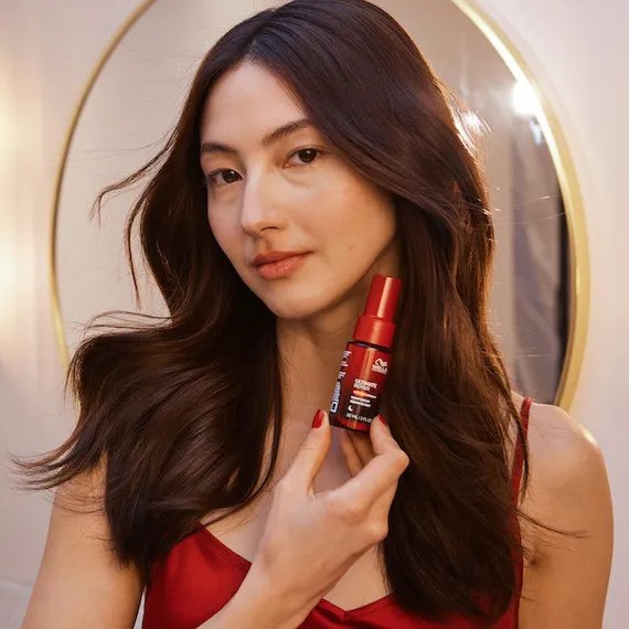 Le mannequin aux cheveux longs, légèrement bouclés et brun foncé tient le sérum de nuit ULTIMATE REPAIR.