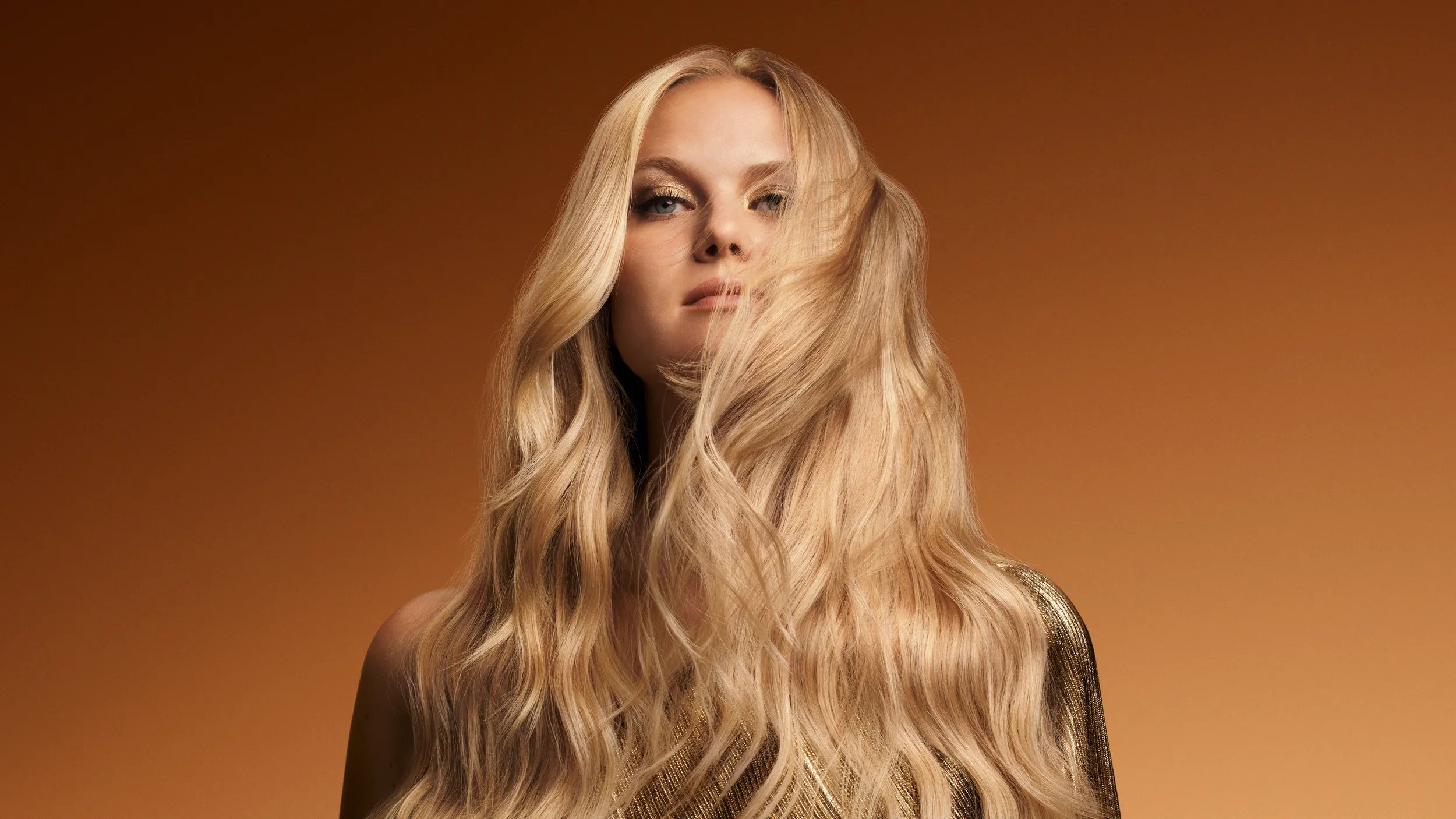 Model with long blonde wavy hair on a golden background. 