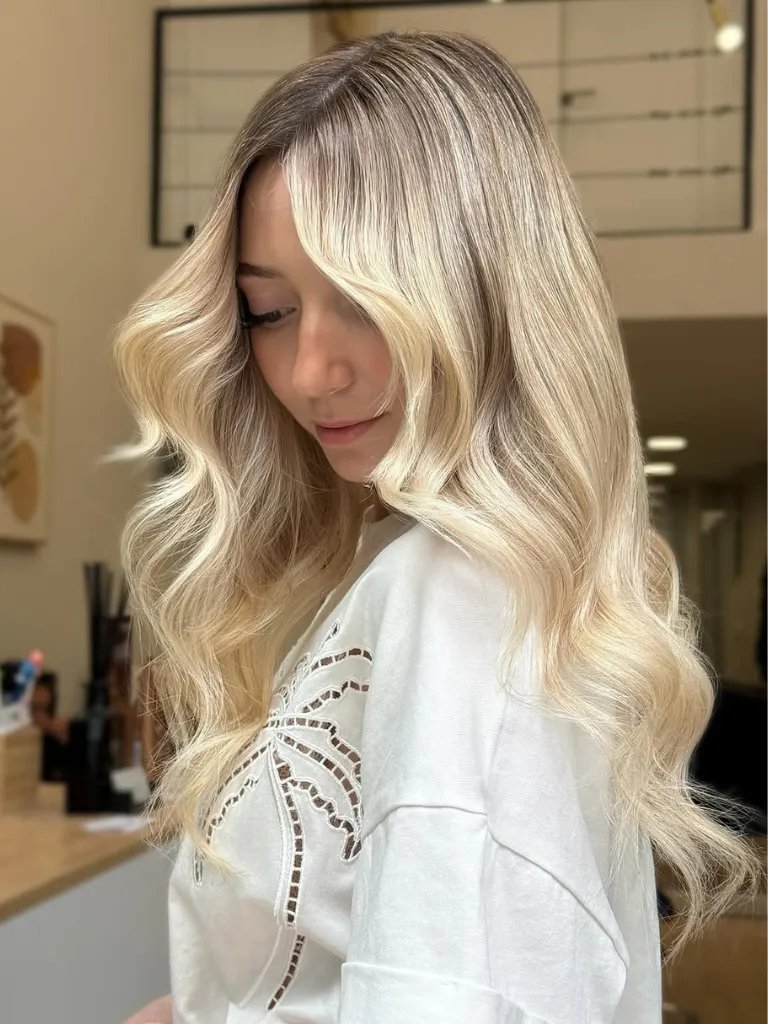 Model with loosely curled, vanilla blonde hair painted in micro-fine highlights.