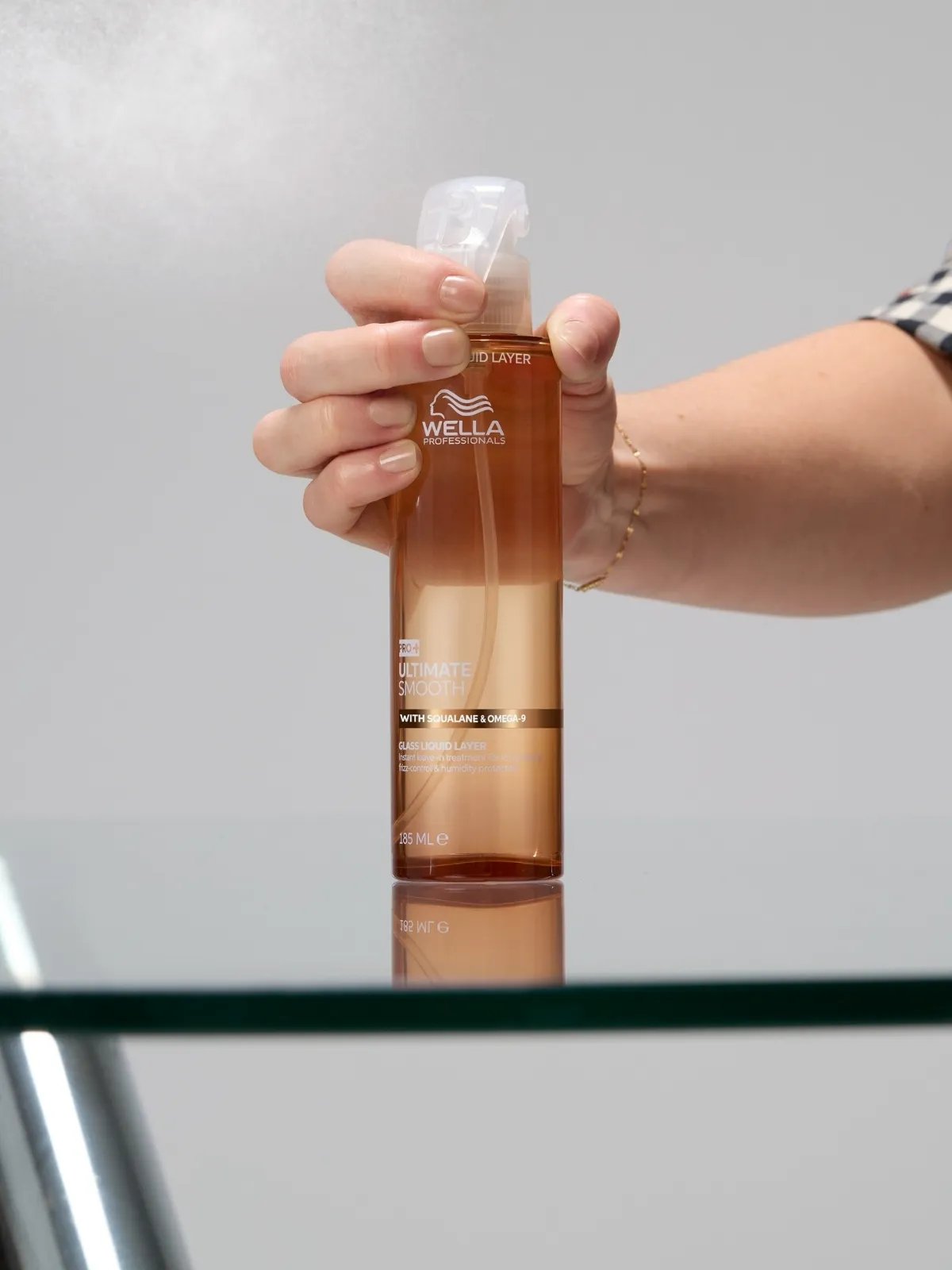 Hairstylist holding the ULTIMATE SMOOTH Glass Liquid Layer spray bottle.