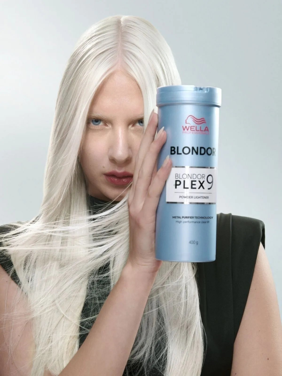 Model with long, straight white blonde hair holds up a tube of BlondorPlex 9.