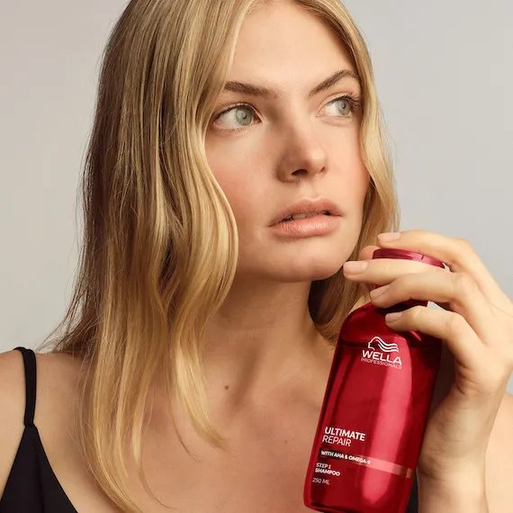 Model with tousled, blonde hair holds ULTIMATE REPAIR Shampoo.