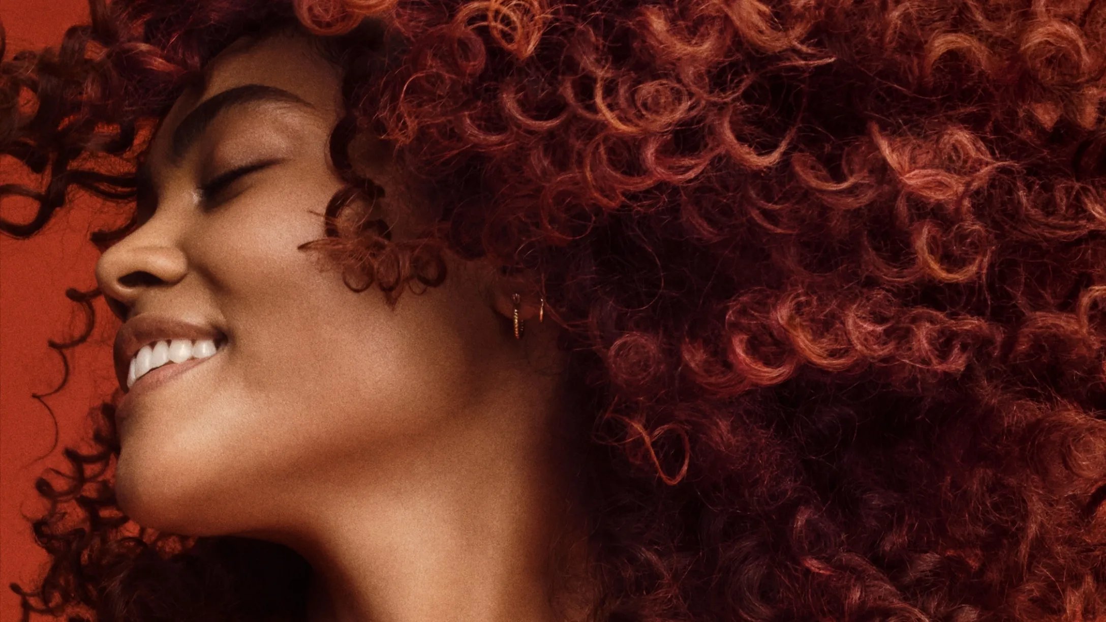 Model swishes their glossy, healthy, curly, brown hair.