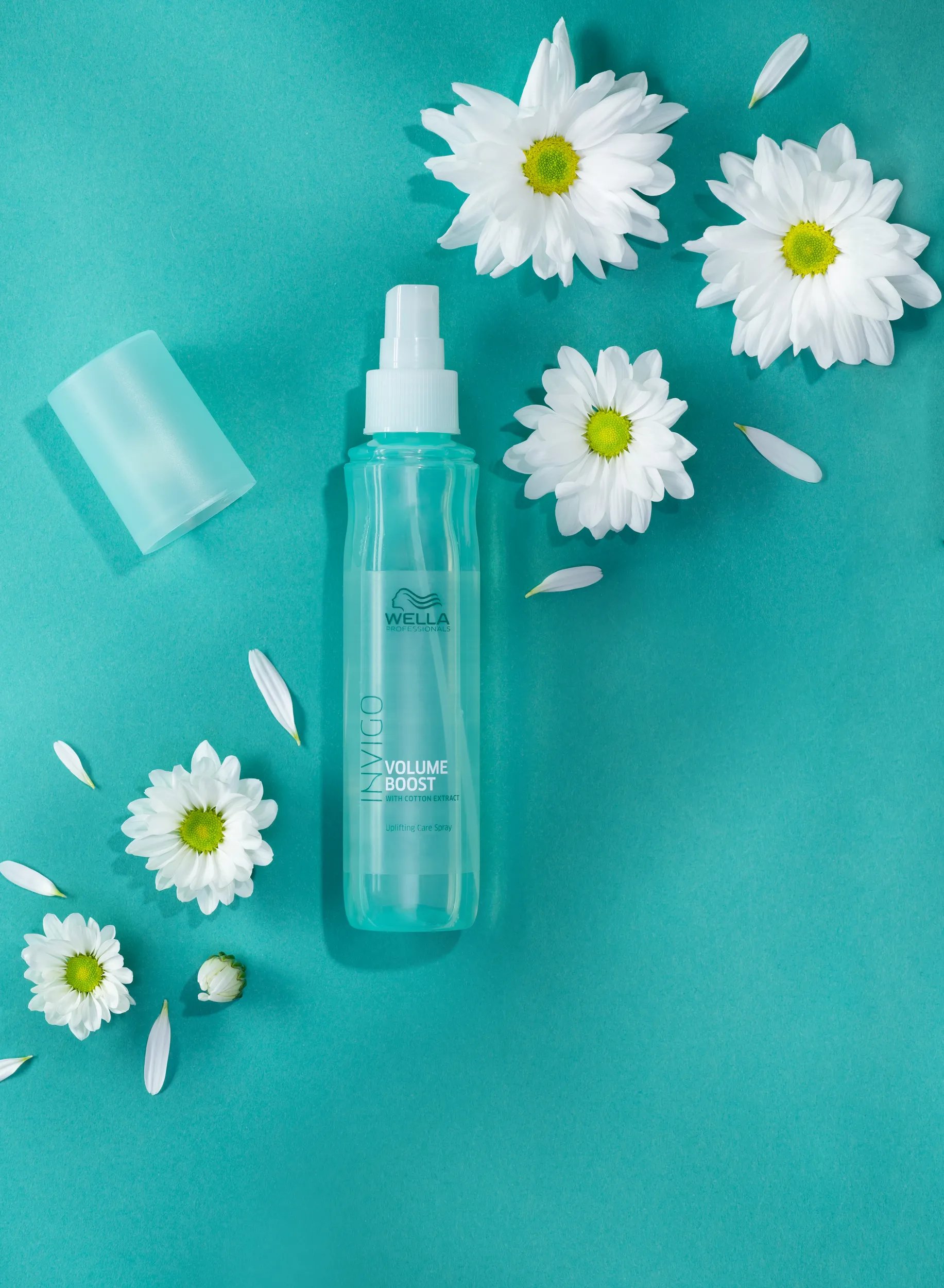 INVIGO Volume Boost Leave-In Spray on a green surface surrounded by flowers.