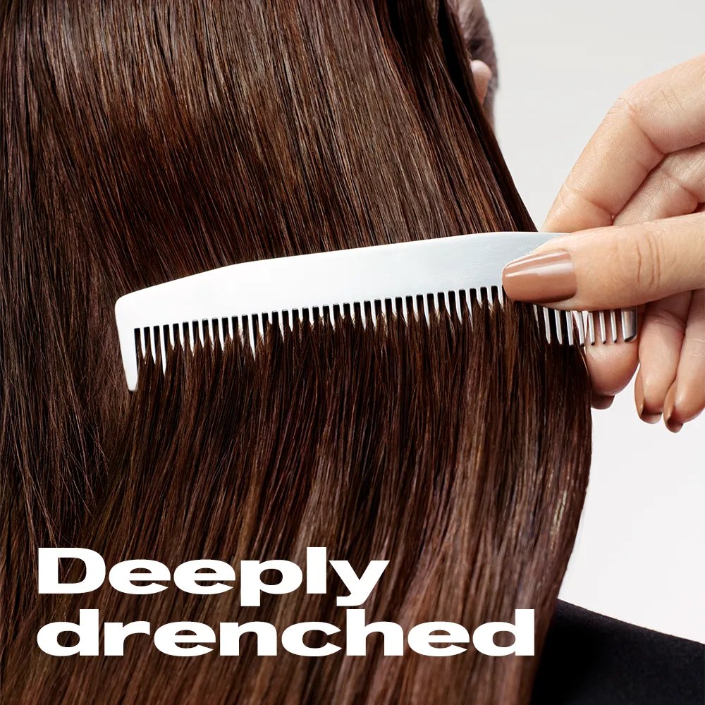 Close-up image of a stylist combing through a model's brunette hair. Text overlay states "Deeply Drenched"