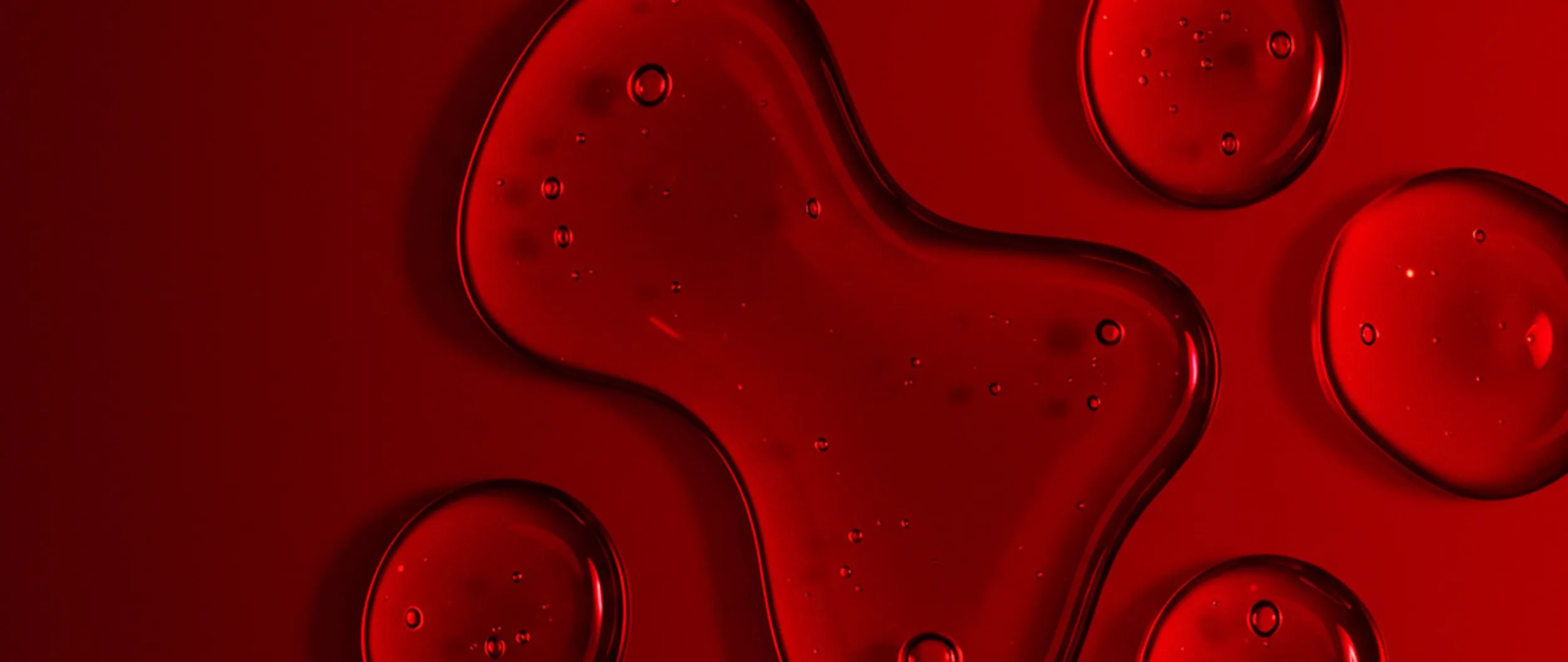 Close-up of clear red liquid droplets and a smear on a textured red surface.