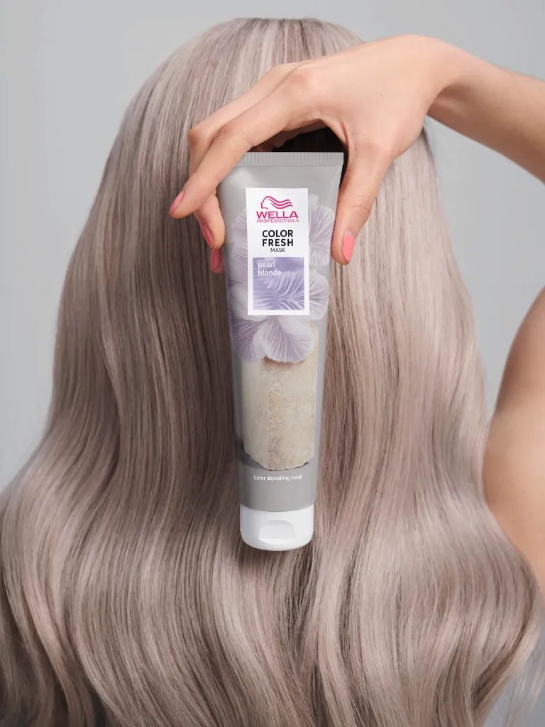 Model with straight, silver blonde hair holds up a tube of Color Fresh Mask in Pearl Blonde.