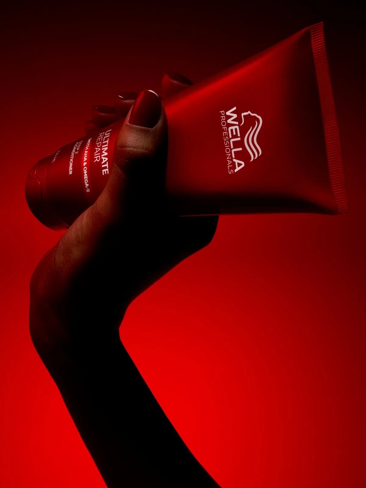 Model holds a bottle of ULTIMATE REPAIR Conditioner against a red backdrop.