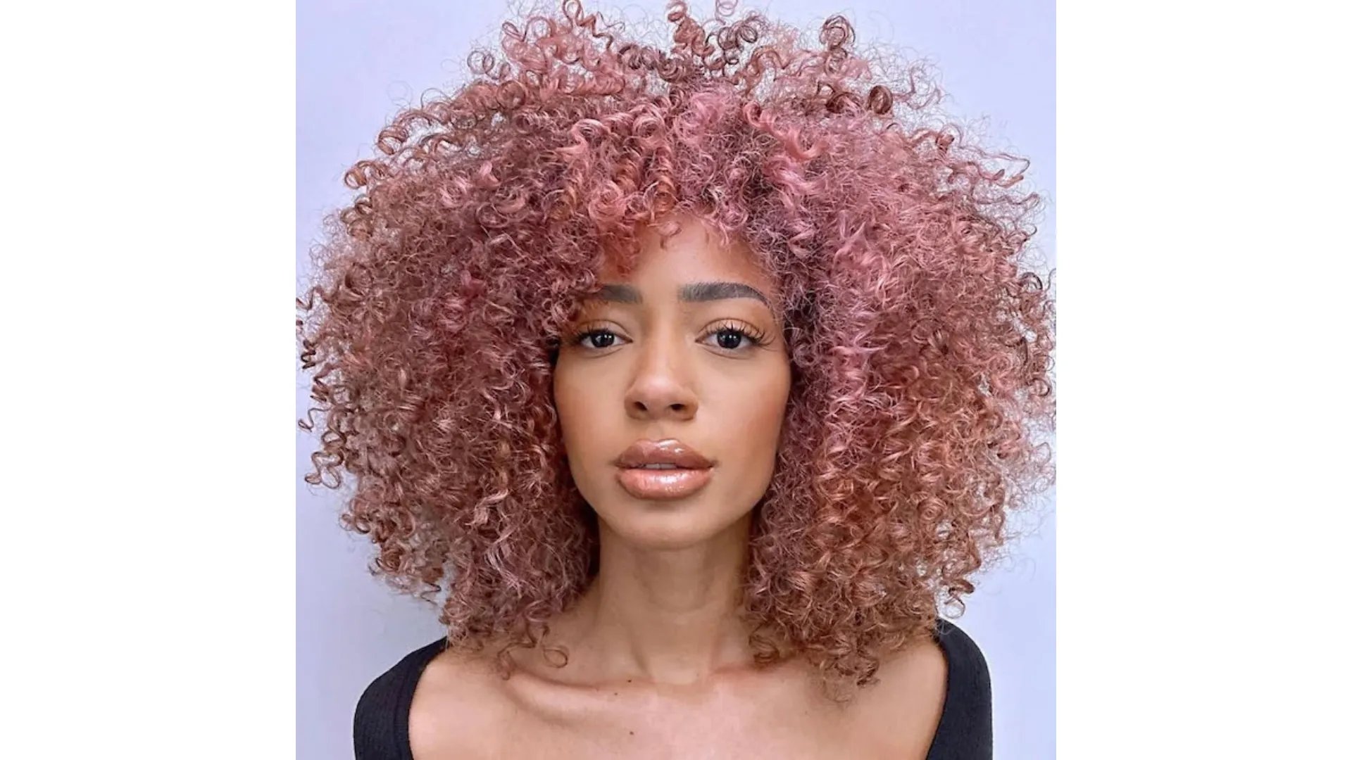 Model with a full head of dusty pink highlights through curly hair.