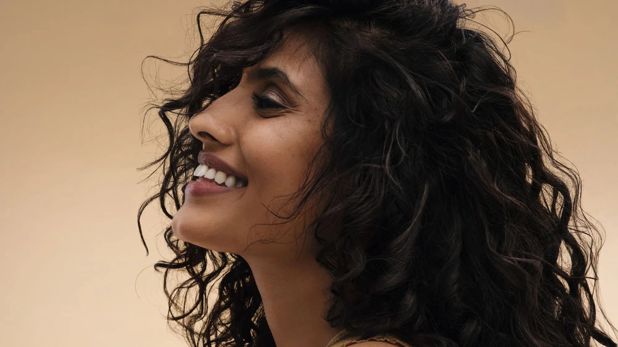 Model with long, dark, wavy hair against a golden backdrop.