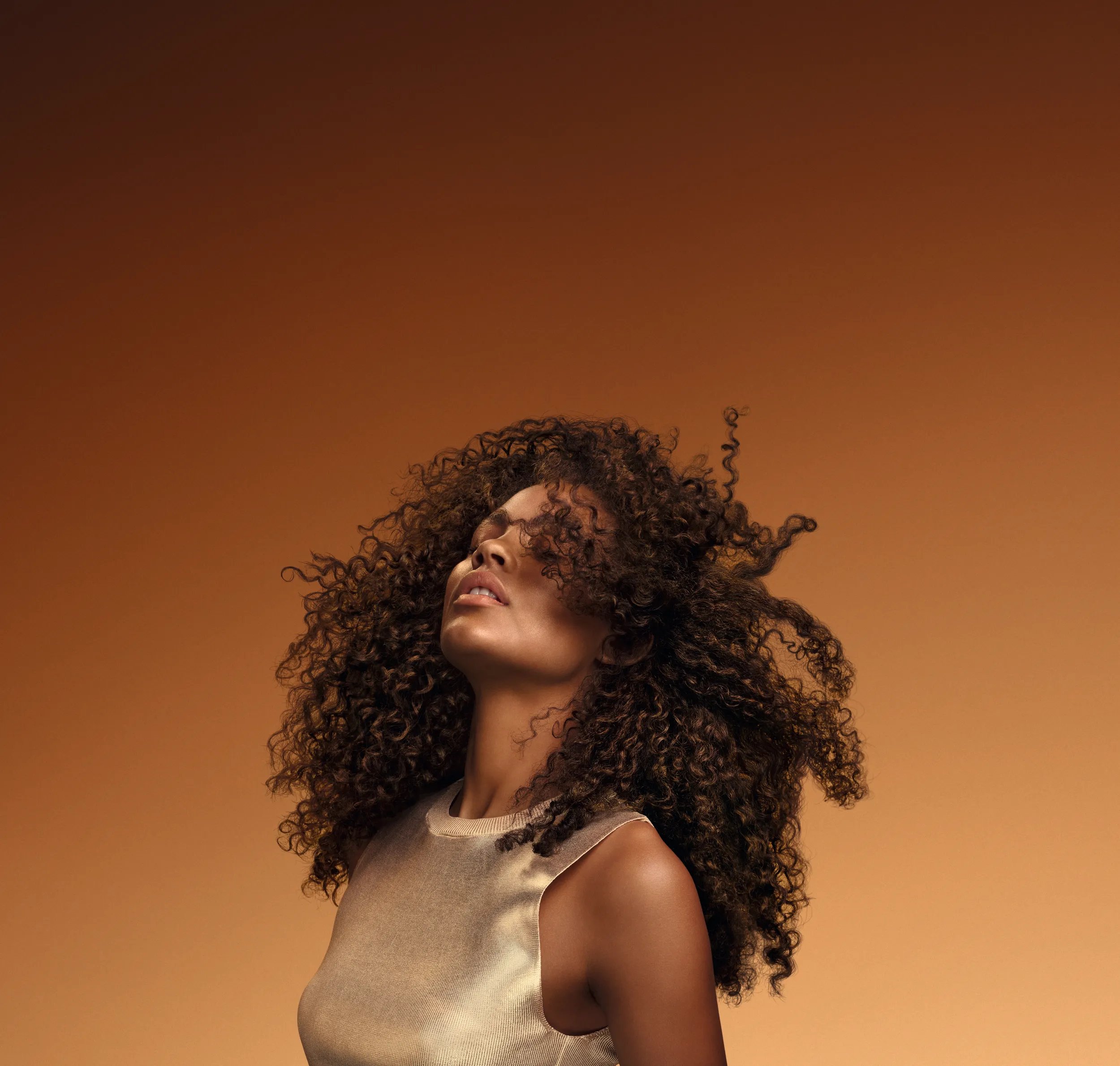 Model tosses their dark brown, glossy, curly hair.