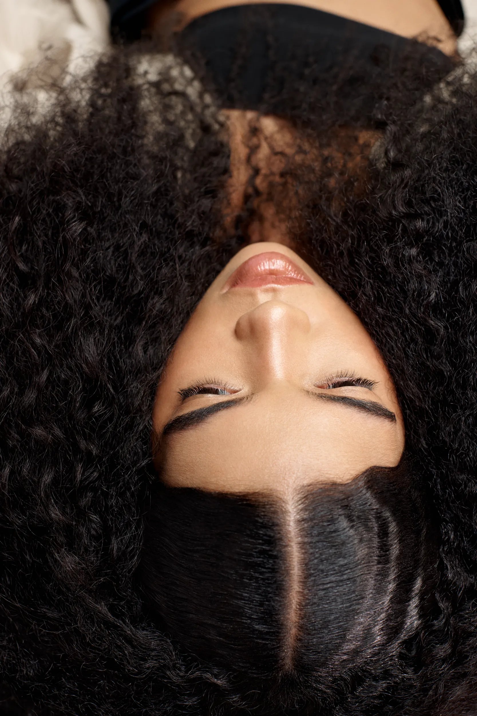 Upside down image of model with big curly hair parted in the middle.