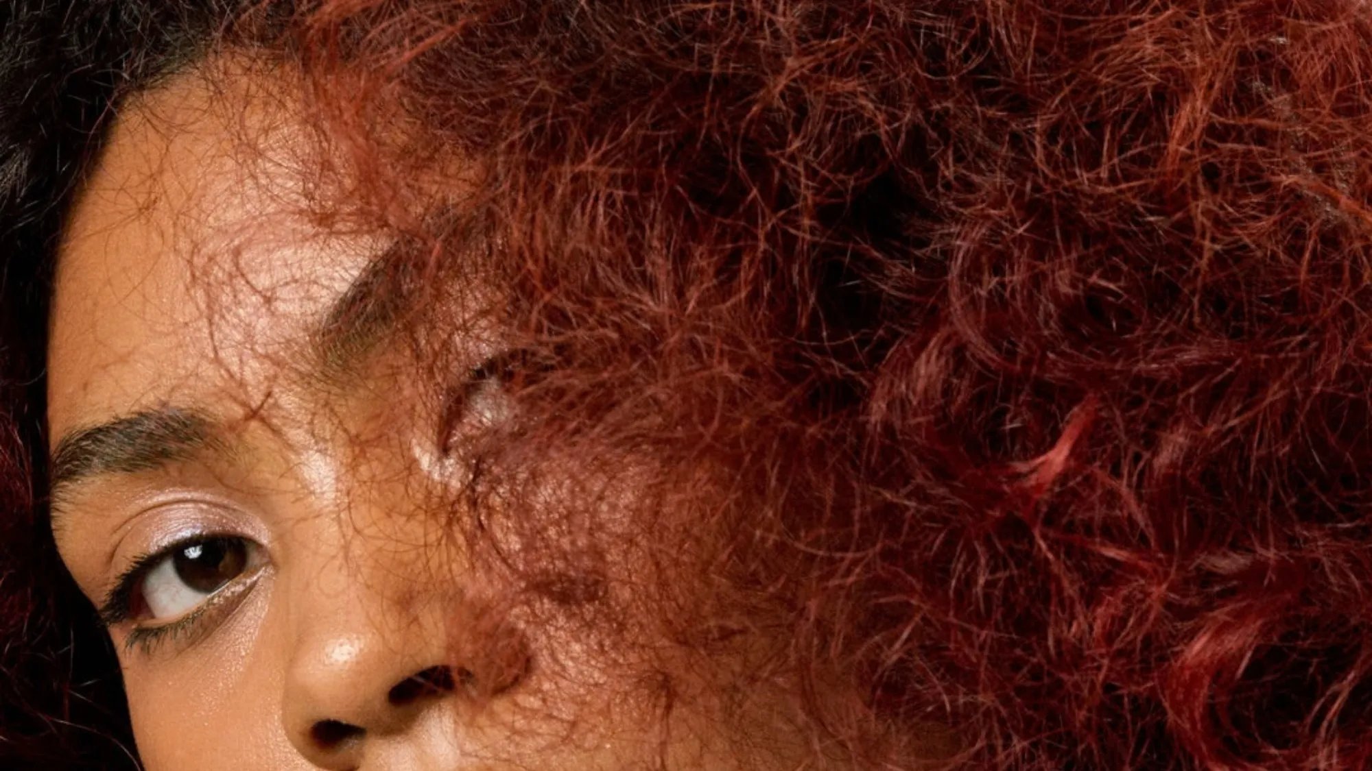 Model with dark brown curly hair featuring red tones.