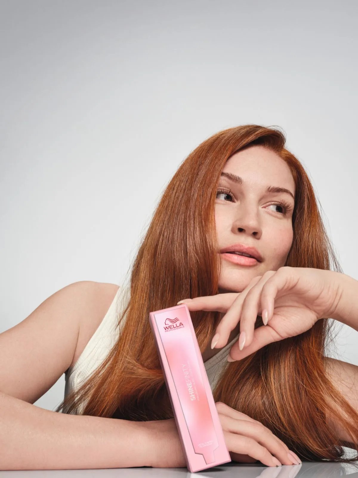Model with vibrant copper hair holds a box of SHINEFINITY.