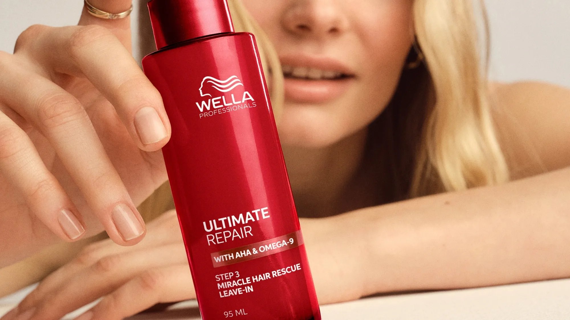 Blonde model holds a bottle of ULTIMATE REPAIR Miracle Hair Rescue.