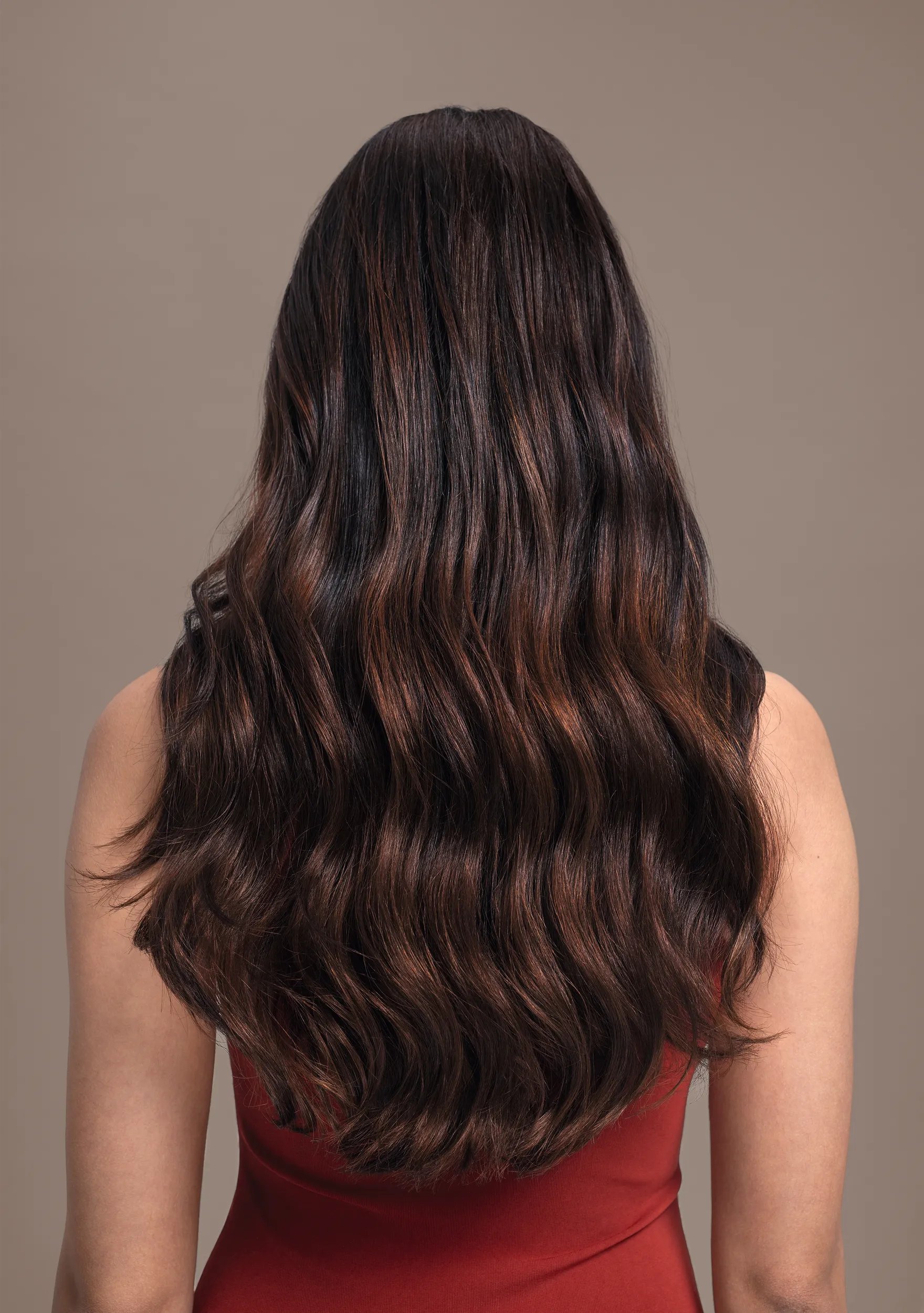 Rückansicht vom Kopf einer Frau mit braunen Haaren, die eine Color Fresh Mask Tube in der Hand hält.