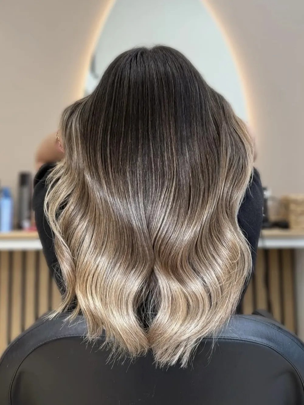 Back view of wavy hair with dark roots blending into cool blonde ends.