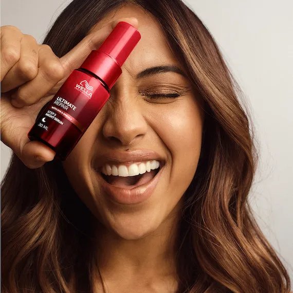 Model with long, brown, wavy hair holds a bottle of ULTIMATE REPAIR Night Serum.