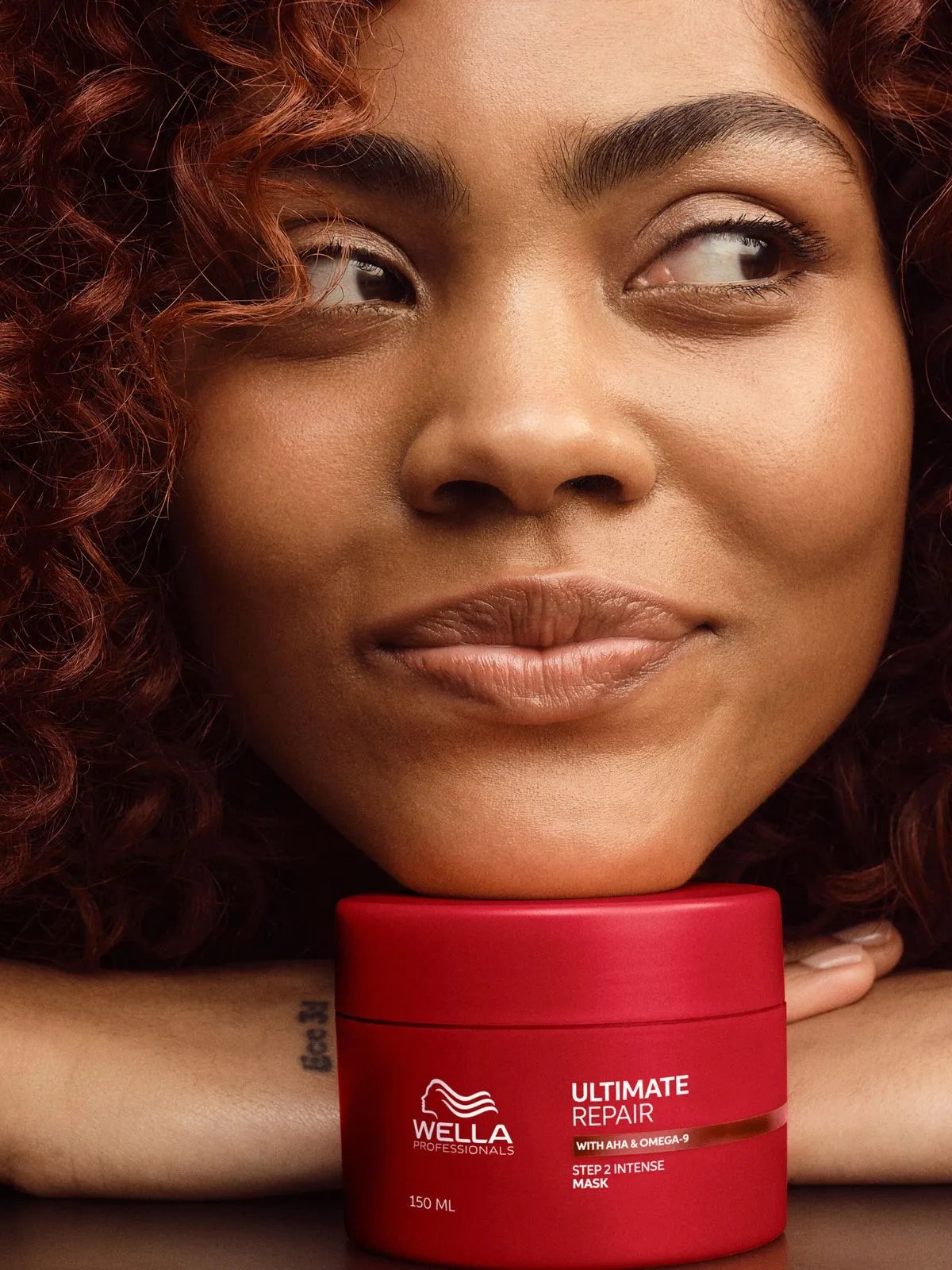 Model with dark brown rests chin on tub of ULTIMATE REPAIR Mask.