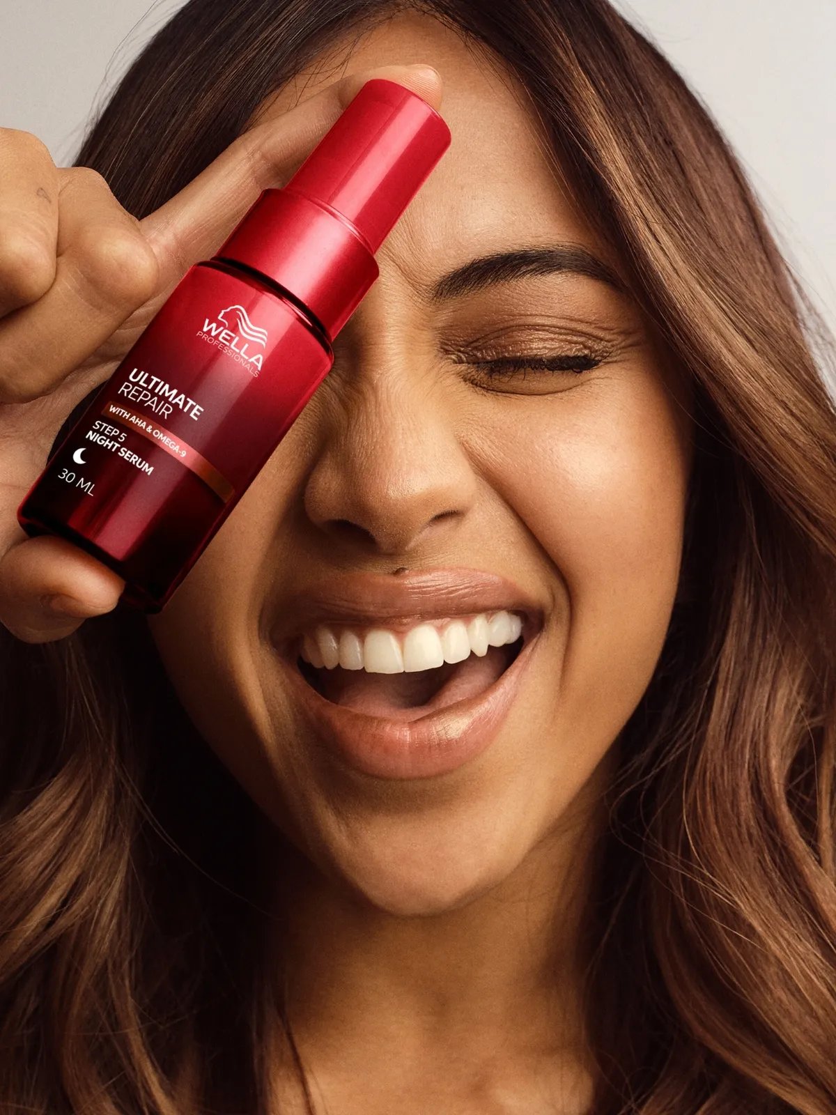 Model with long, loosely curled, brown hair holds up ULTIMATE REPAIR Night Serum.