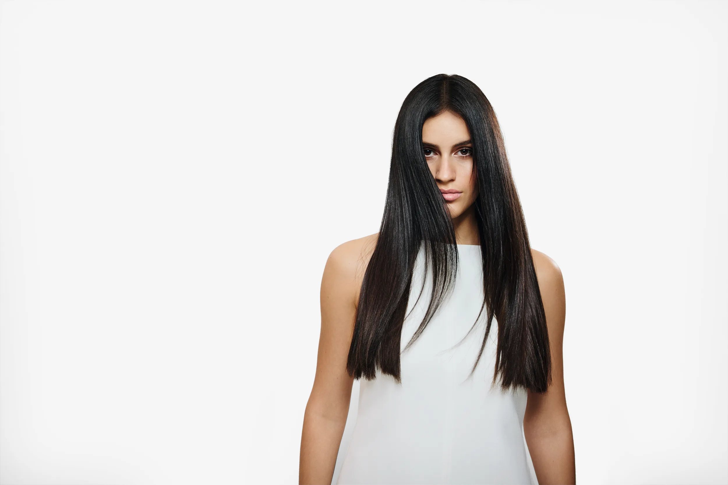 A model with long, straight black hair wearing a white top against a plain white background.