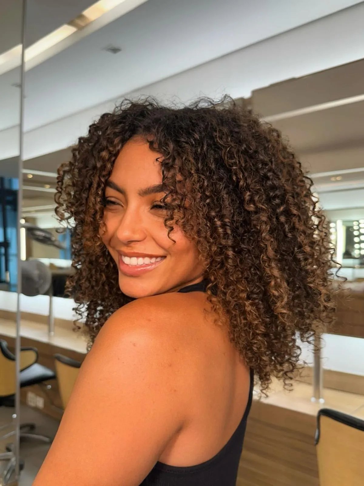 Model with dark brown, curly, shiny hair glances over shoulder.