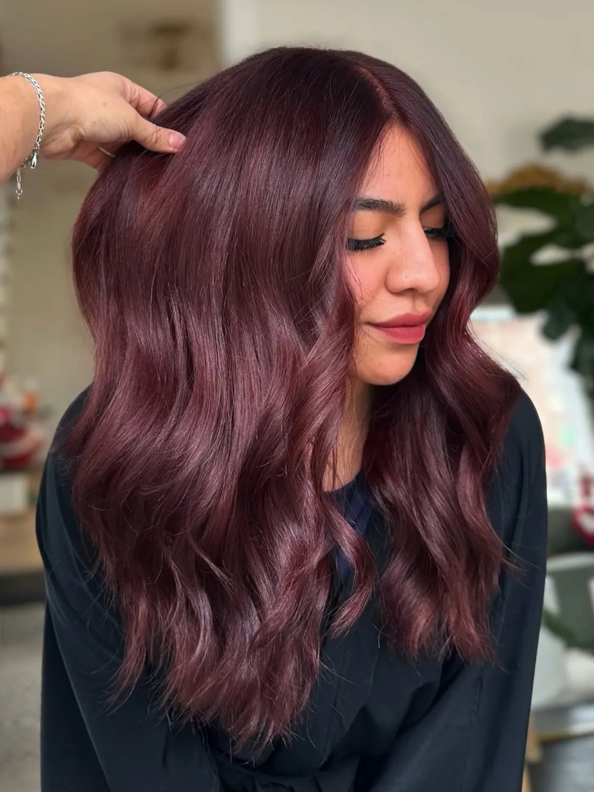 Model with wavy, cool-toned maroon red hair.