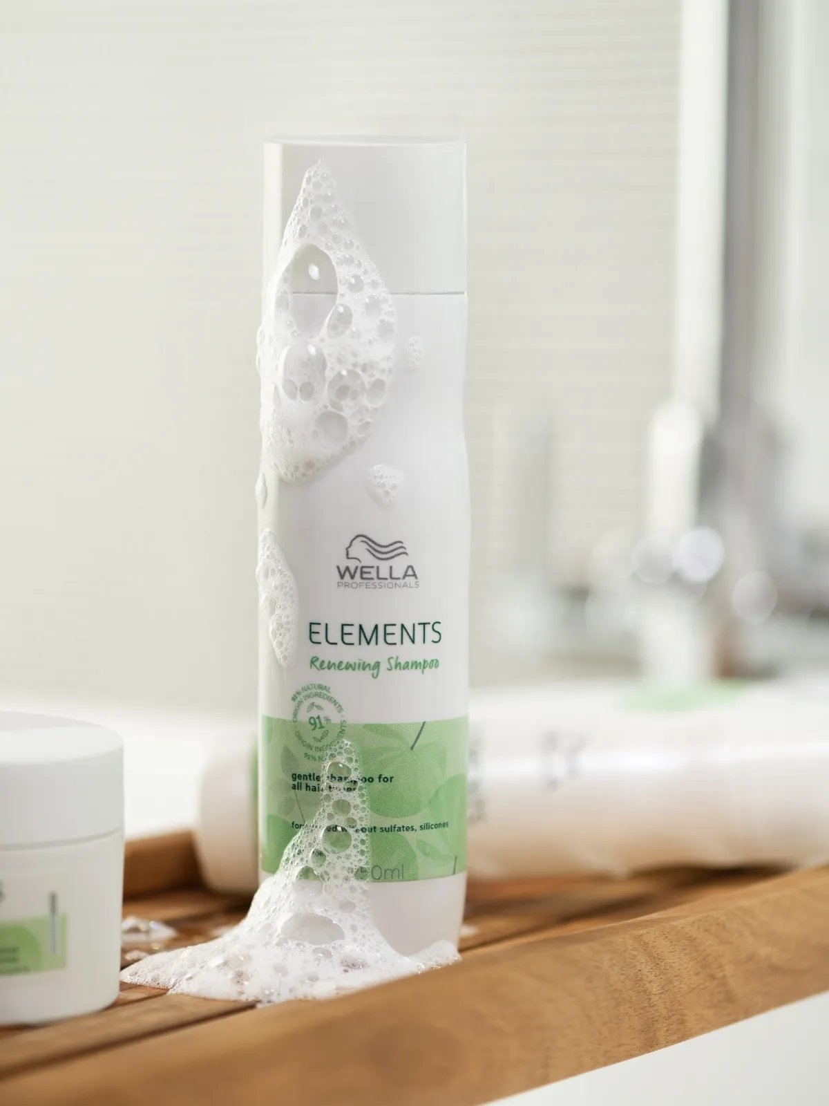 Elements Renewing Shampoo on a wooden shelf, with foam running down the bottle.