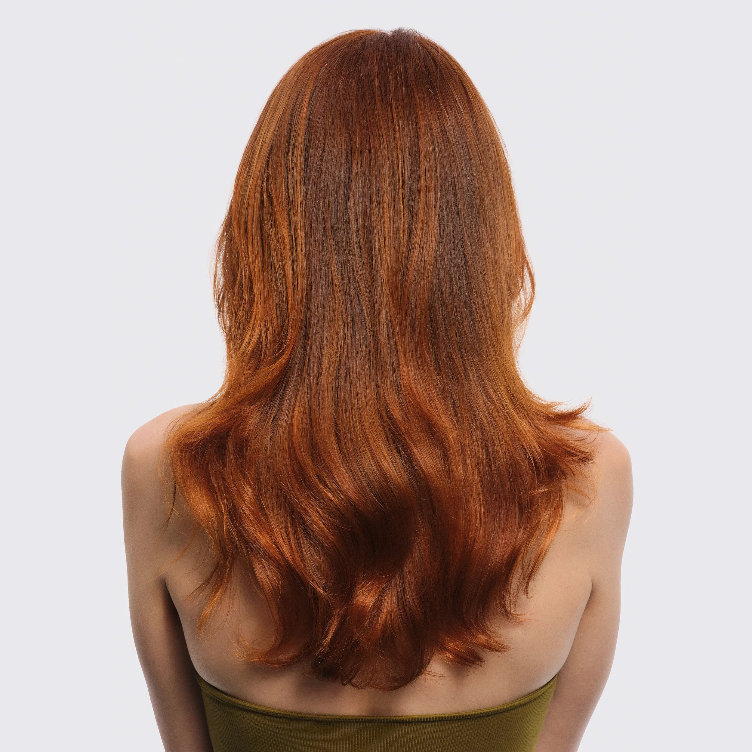 Εικόνα μοντέλου με γυρισμένη την πλάτη, μπροστά από λευκό φόντο. Τα μαλλιά του μοντέλου είναι κόκκινα, κυμματιστά μεσαίου μήκους. Το μοντέλο φοράει ένα πράσινο τοπ.