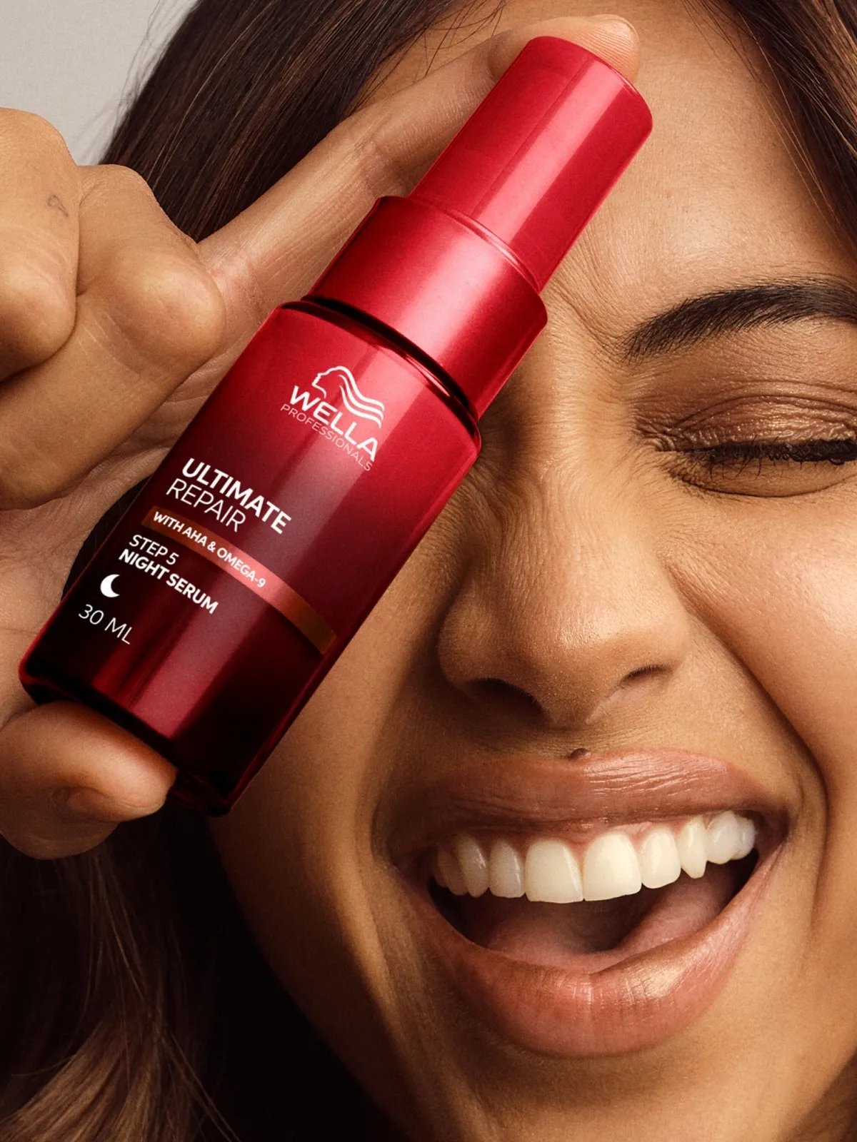 Model holds ULTIMATE REPAIR Night Serum in front of one eye.