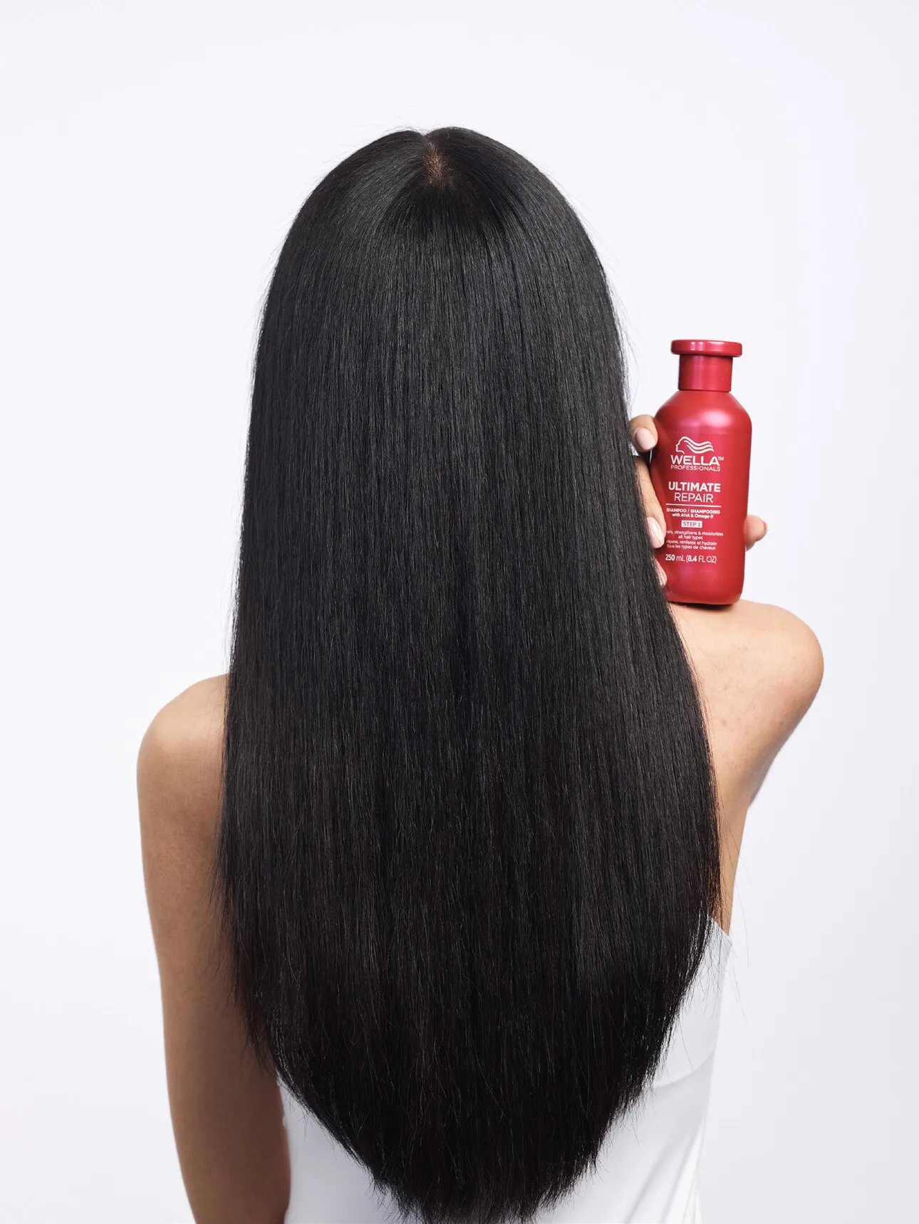 Arrière de la tête du modèle avec de longs cheveux noirs et raides. Ils tiennent un flacon de shampooing Ultimate Repair.