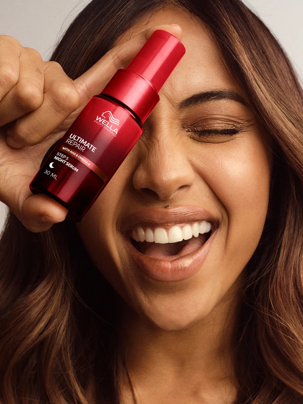 Model with long, brown, wavy hair holds a bottle of ULTIMATE REPAIR Night Serum.