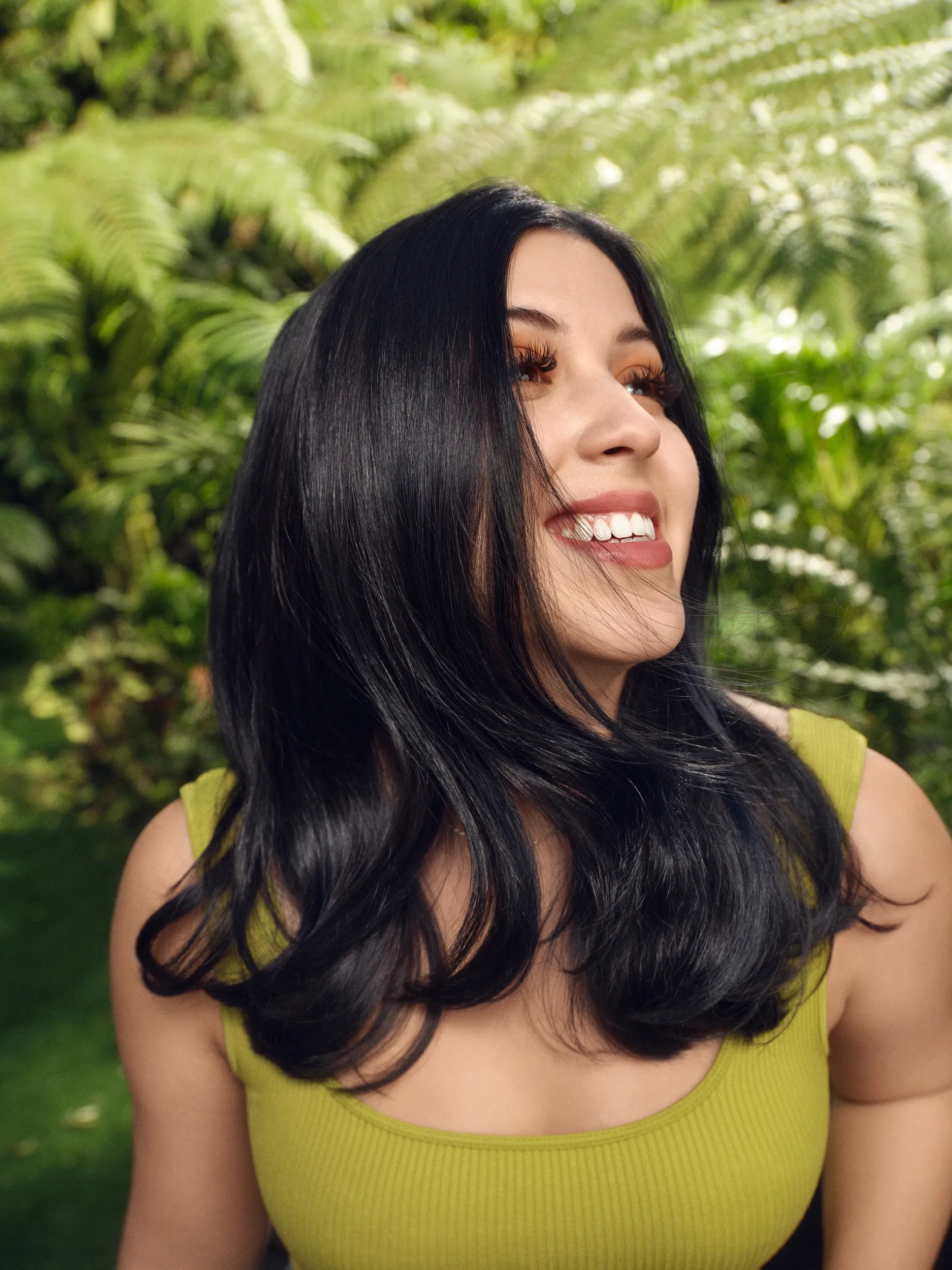 Sofia Bella with long black hair in a green outfit against the background of rich vegetation