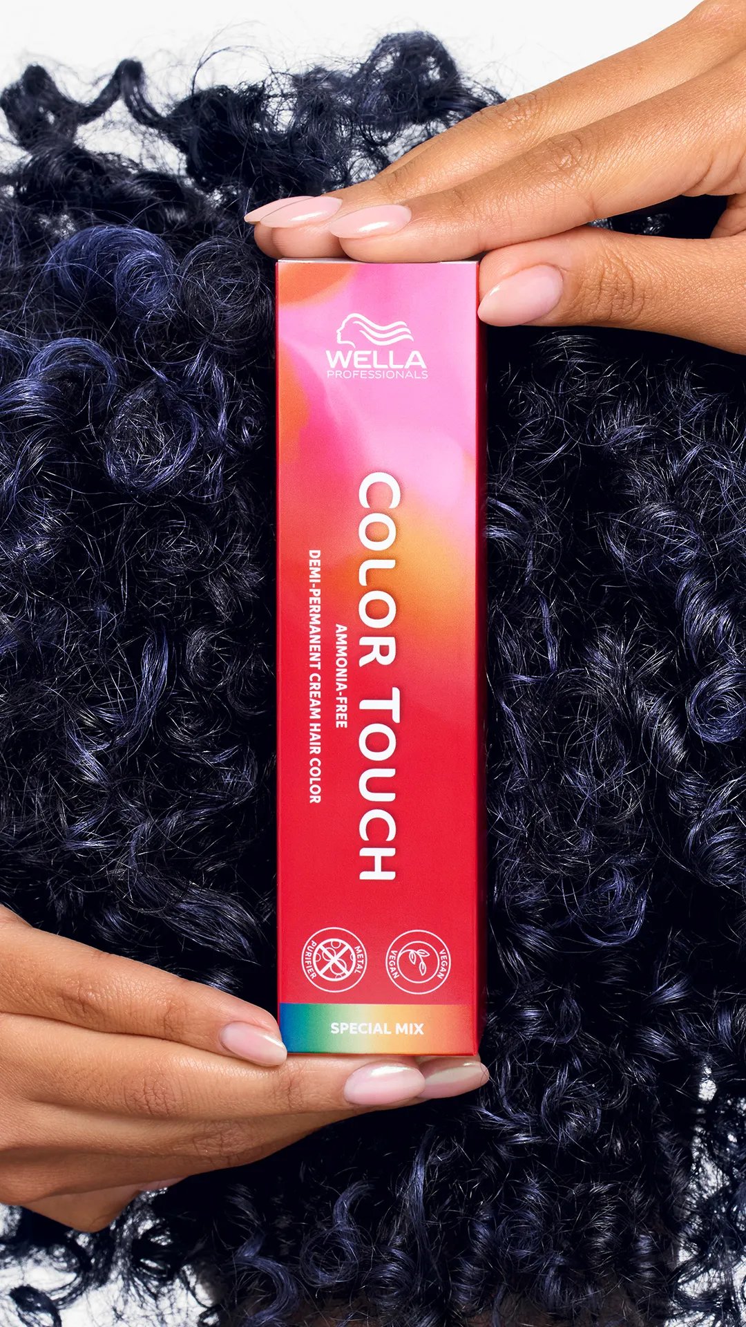 Model with dark blue, curly hair holds up a box of Color Touch.