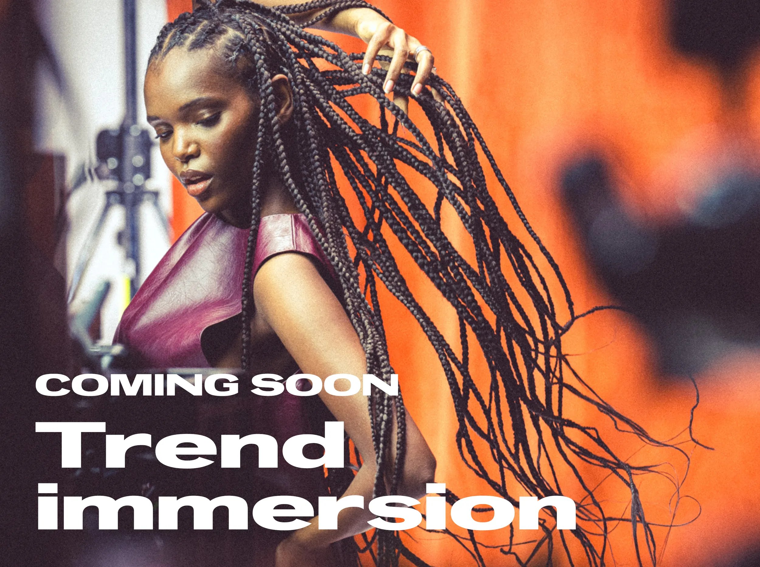 Immagine di una modella girata di lato con lunghe trecce brune. Il testo in sovrimpressione recita “In arrivo Trend Immersion"
