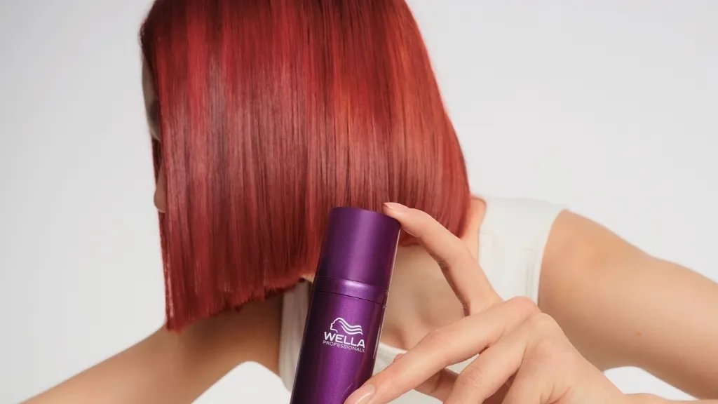 Model with red hair holds a bottle of ULTIMATE COLOR Miracle Leave-In Mask.