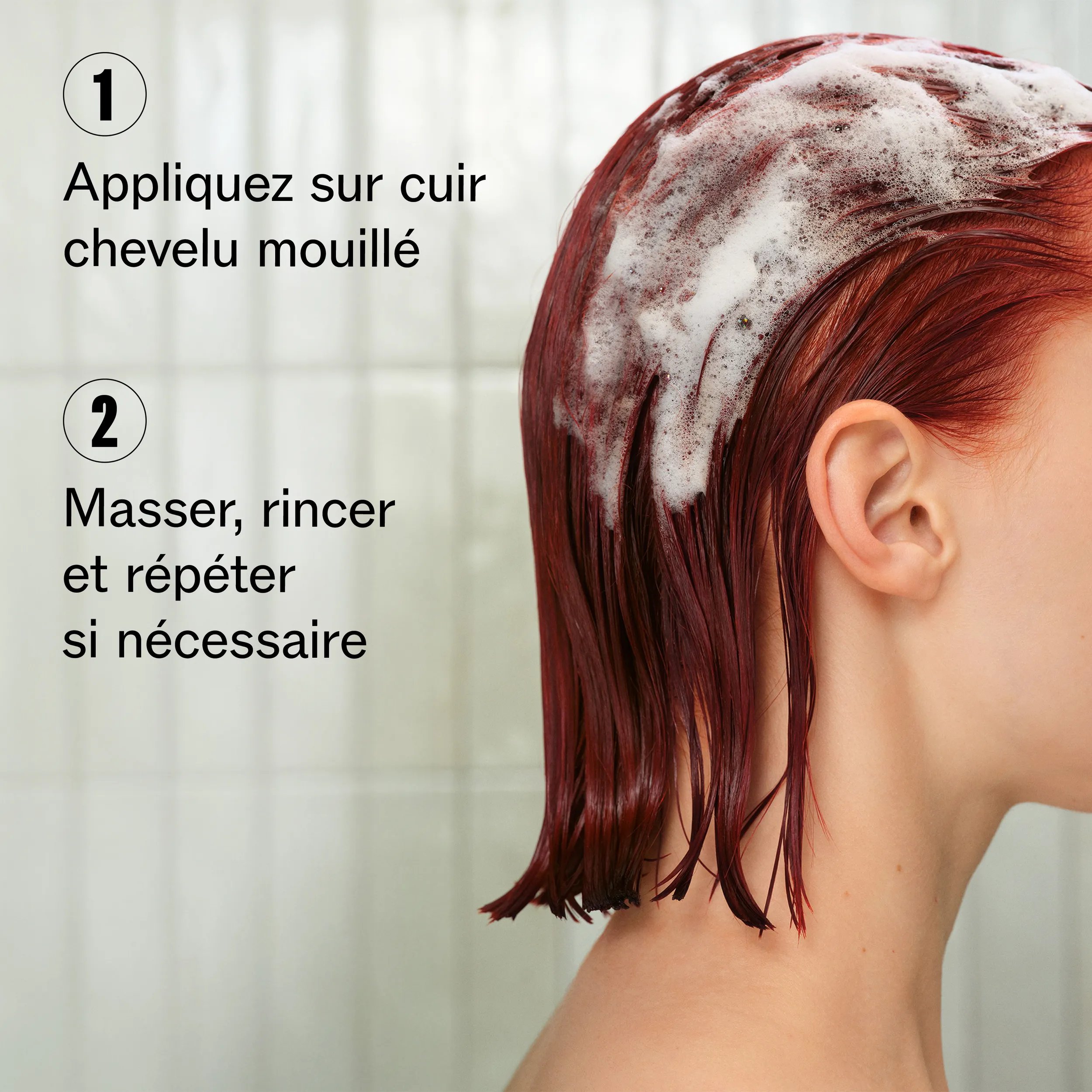 Image en profil d’un modèle, cadrée pour ne pas montrer le visage. Les cheveux du modèle sont rouges, courts et mouillés, recouverts de mousse de shampoing.
Une incrustation de texte indique :
« 1. Appliquer sur cheveux et cuir chevelu mouillé.
2. Masser, rincer et répéter si nécessaire. »