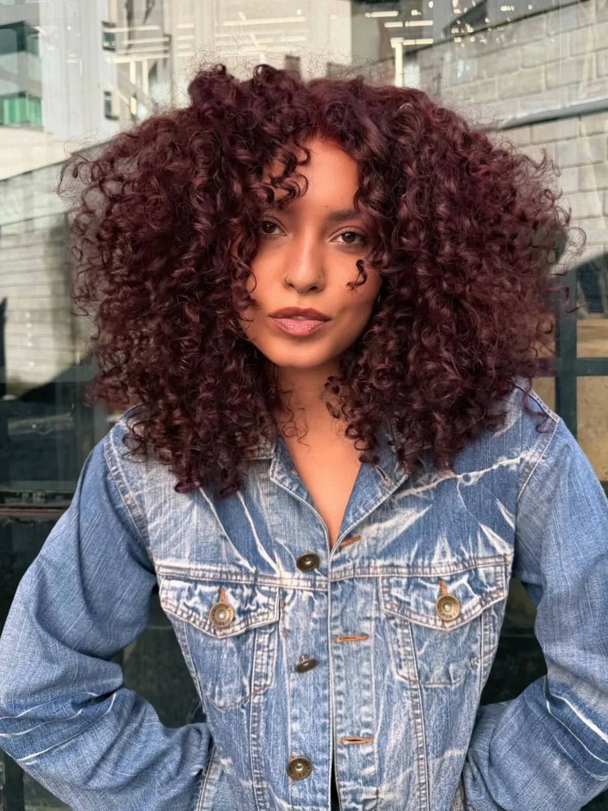 Model with glossy, curly hair in a burgundy red shade.