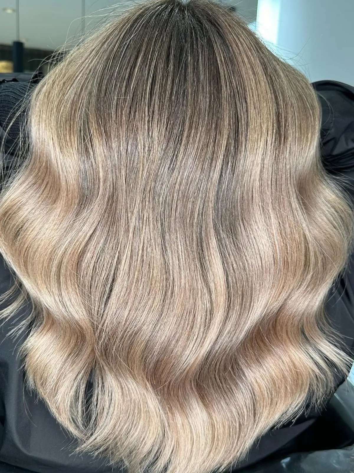 Model with shoulder-length, wavy ash blonde hair and a dark root shadow.