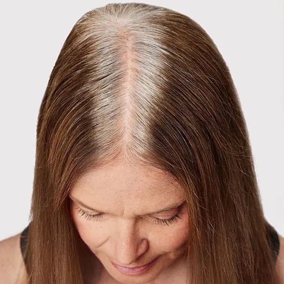 Close-up of model’s white and gray roots against light brown hair.