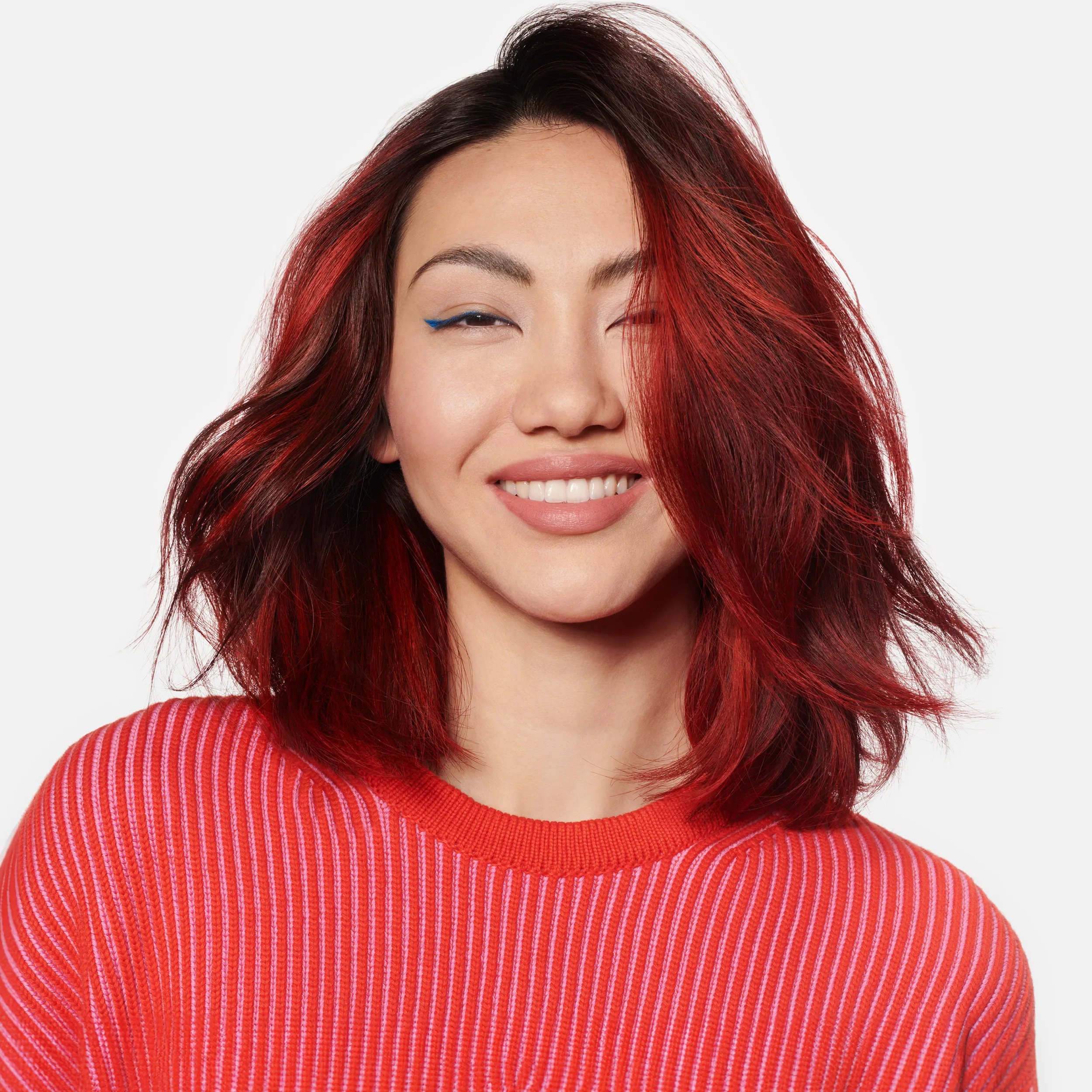 A model with shoulder-length, black and red hair smiles into the camera.