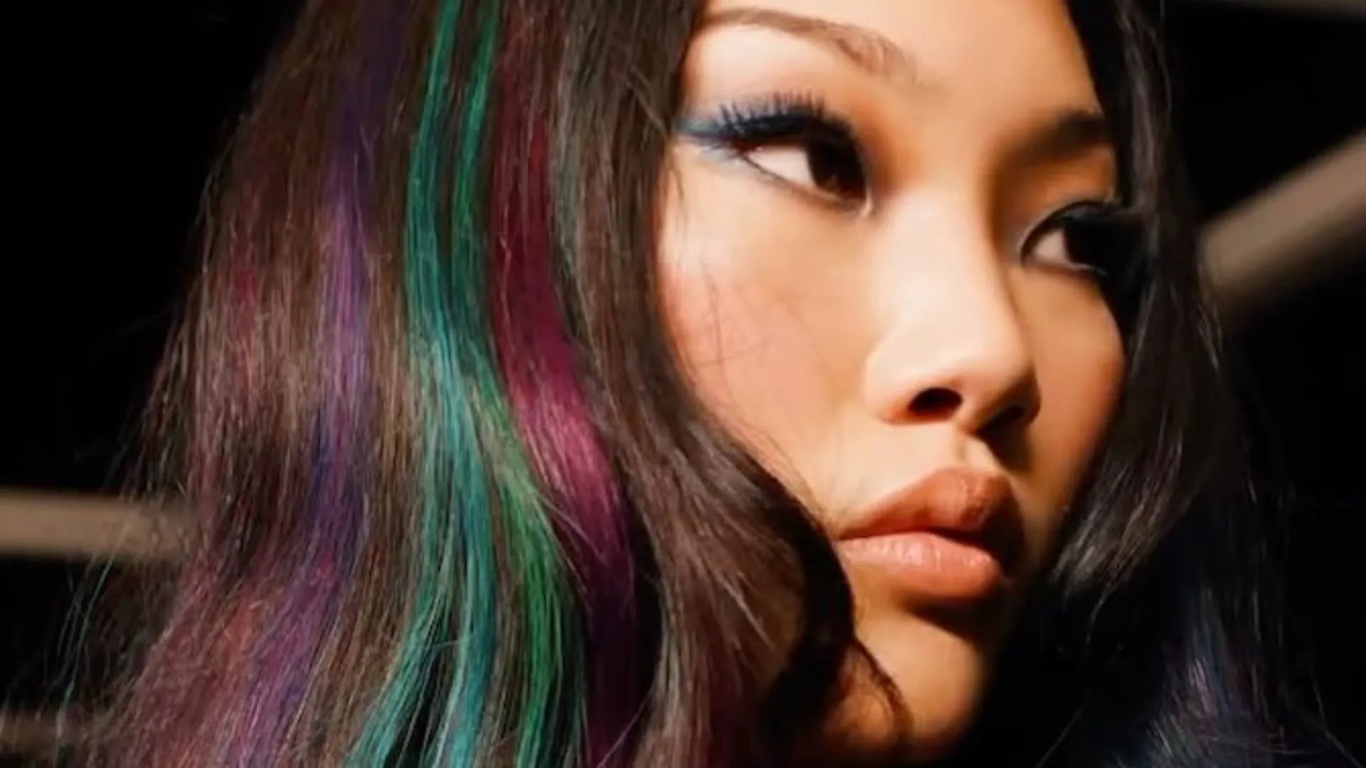 Model with dark brown hair featuring teal and violet highlights.
