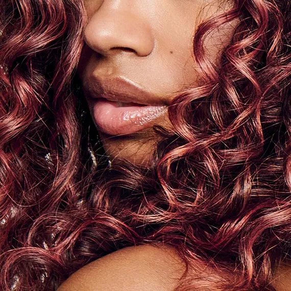Model with curly, dark brown hair featuring coral highlights.