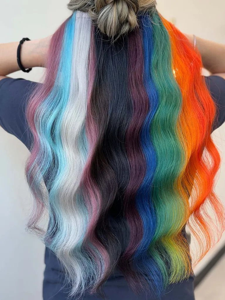 Model’s long, wavy hair is painted in colors from the Progress Pride flag, including pastel tones and bold brights.