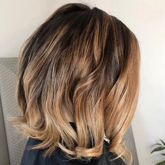 Model running their hand through their shoulder-length, light brown, wavy hair.