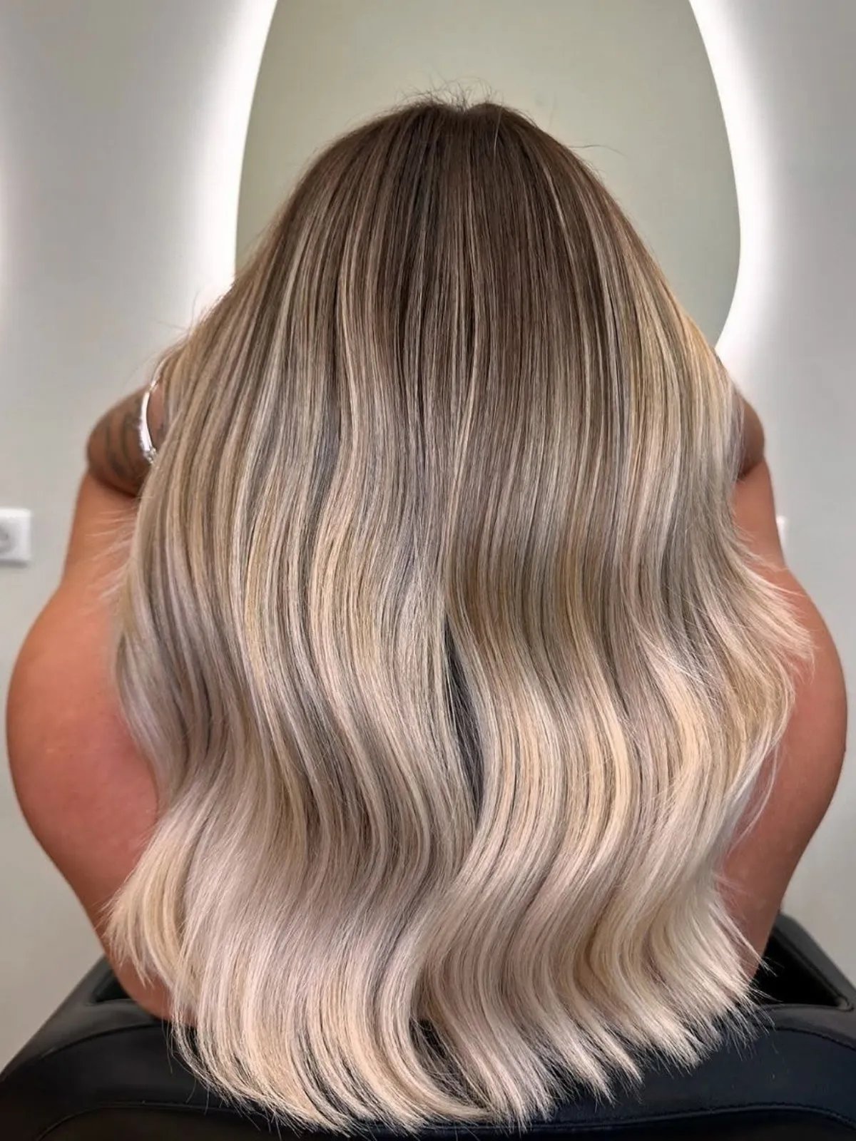 Back of model’s head showing a pearl blonde balayage with darker roots.