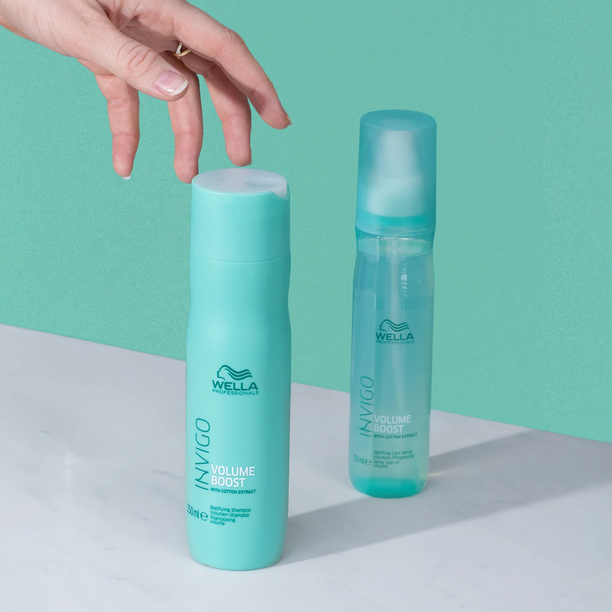 Product shot of the Wella Professionals Invigo Volume Boost line, including the shampoo and care spray, against a light turquoise background