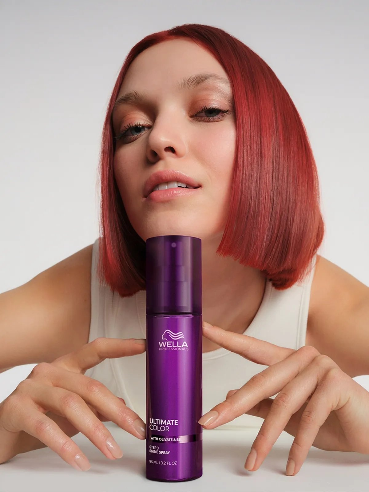 Red-haired model rests chin on a bottle of ULTIMATE COLOR Shine Spray.